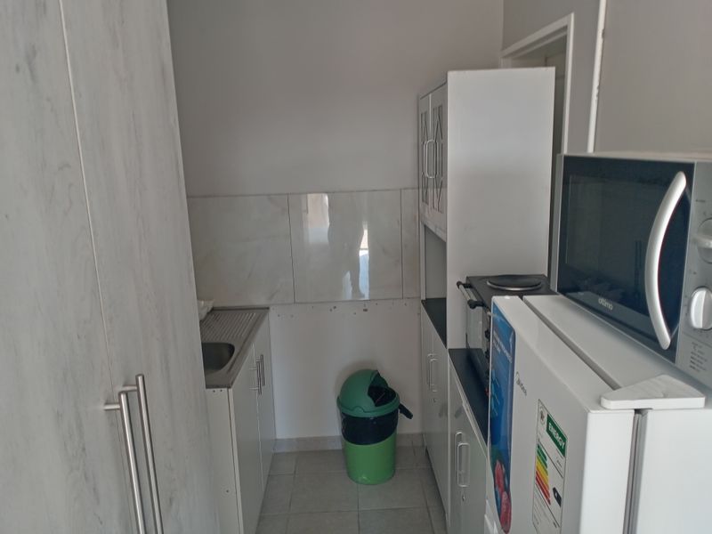 A compact scullery area featuring built-in cabinetry, a stainless steel sink, and tiled splashback, providing functional utility space for the home.