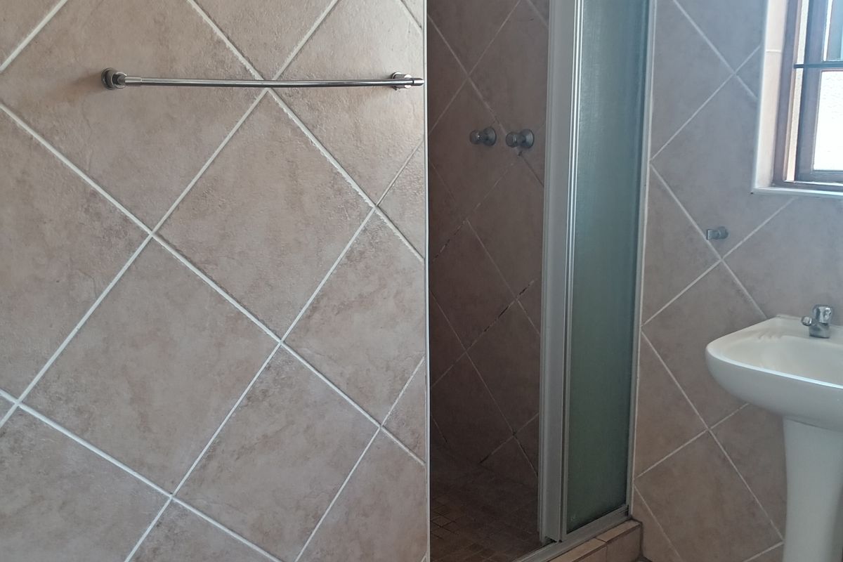 A functional bathroom featuring a shower enclosure, pedestal basin, and neutral ceramic tiling throughout.