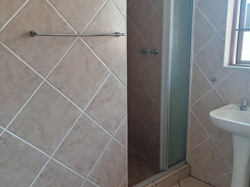 A functional bathroom featuring a shower enclosure, pedestal basin, and neutral ceramic tiling throughout.