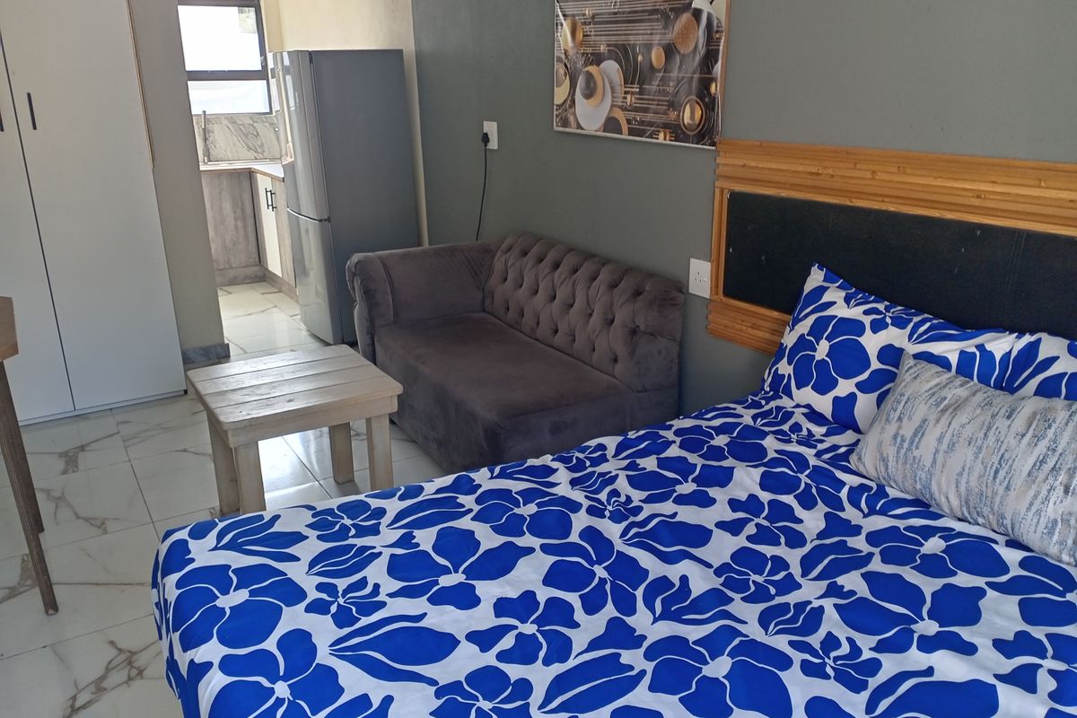 A bedroom featuring tiled flooring and a built-in wardrobe, with an adjacent view into a small kitchen area.