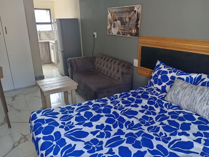 A bedroom featuring tiled flooring and a built-in wardrobe, with an adjacent view into a small kitchen area.