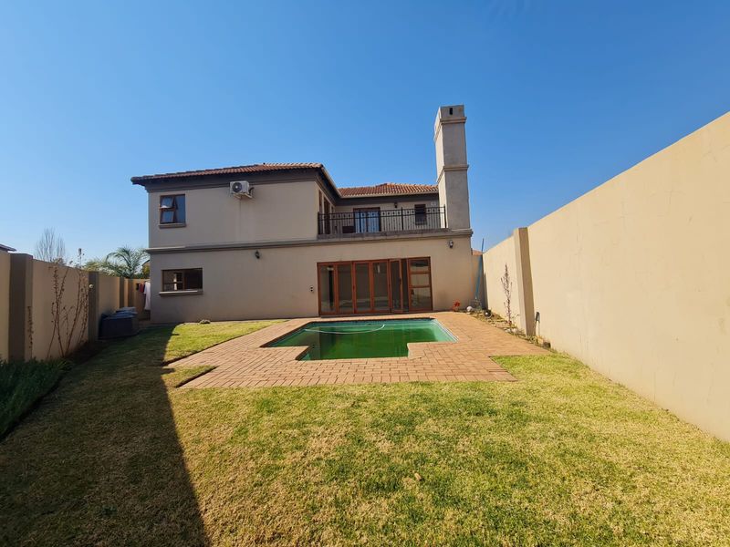 Rear view of the property featuring a swimming pool, paved surround, lawn, and a balcony accessible from the upper level.