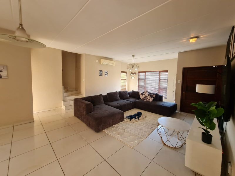 Spacious living room featuring neutral tiled flooring, a split-system air conditioner, and a staircase leading to the upper level.