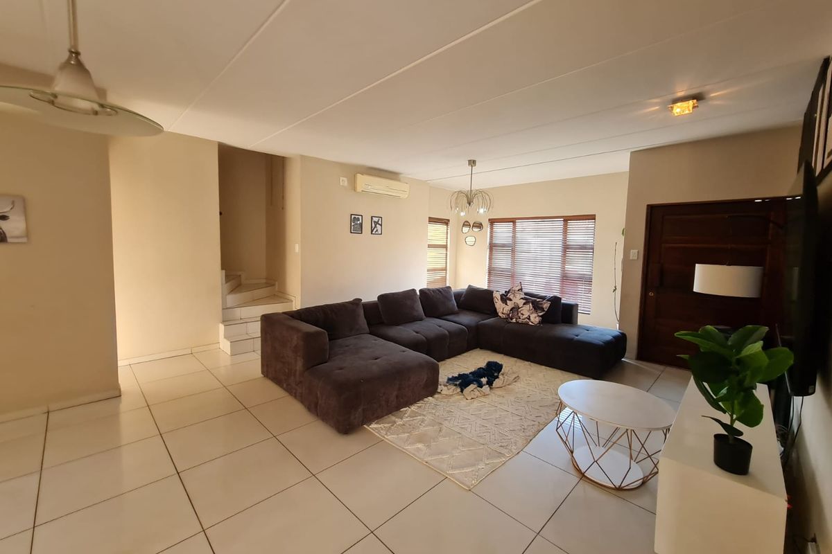 Spacious living room featuring neutral tiled flooring, a split-system air conditioner, and a staircase leading to the upper level.
