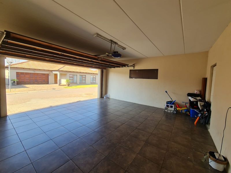 A spacious, clean garage featuring tiled flooring, an automated door mechanism, and a horizontal window, providing ample space for vehicle storage.