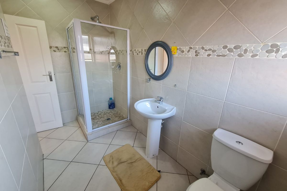 A clean and functional bathroom featuring a pedestal basin, a glass-enclosed shower, and a standard toilet with neutral wall and floor tiling.