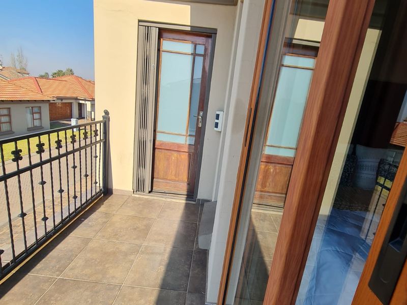 A well-maintained balcony featuring tiled flooring, a secure wrought iron balustrade, and access via a sliding glass door and a timber-framed door.