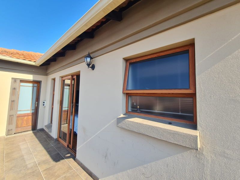 A covered patio area featuring tiled flooring, wooden-framed sliding doors, and a matching top-hung window, providing a clean and functional outdoor transition space.