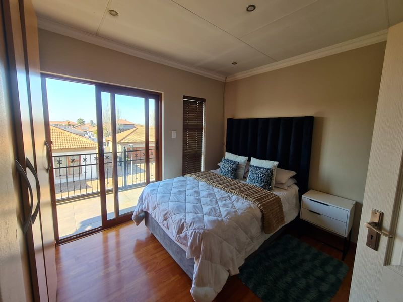 A well-lit bedroom featuring laminate flooring, built-in wardrobes, and a sliding glass door providing direct access to a private balcony.