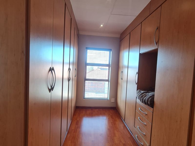 A walk-in dressing area or bedroom featuring extensive floor-to-ceiling built-in wooden cabinetry, laminate flooring, and natural light from a window with fitted blinds.