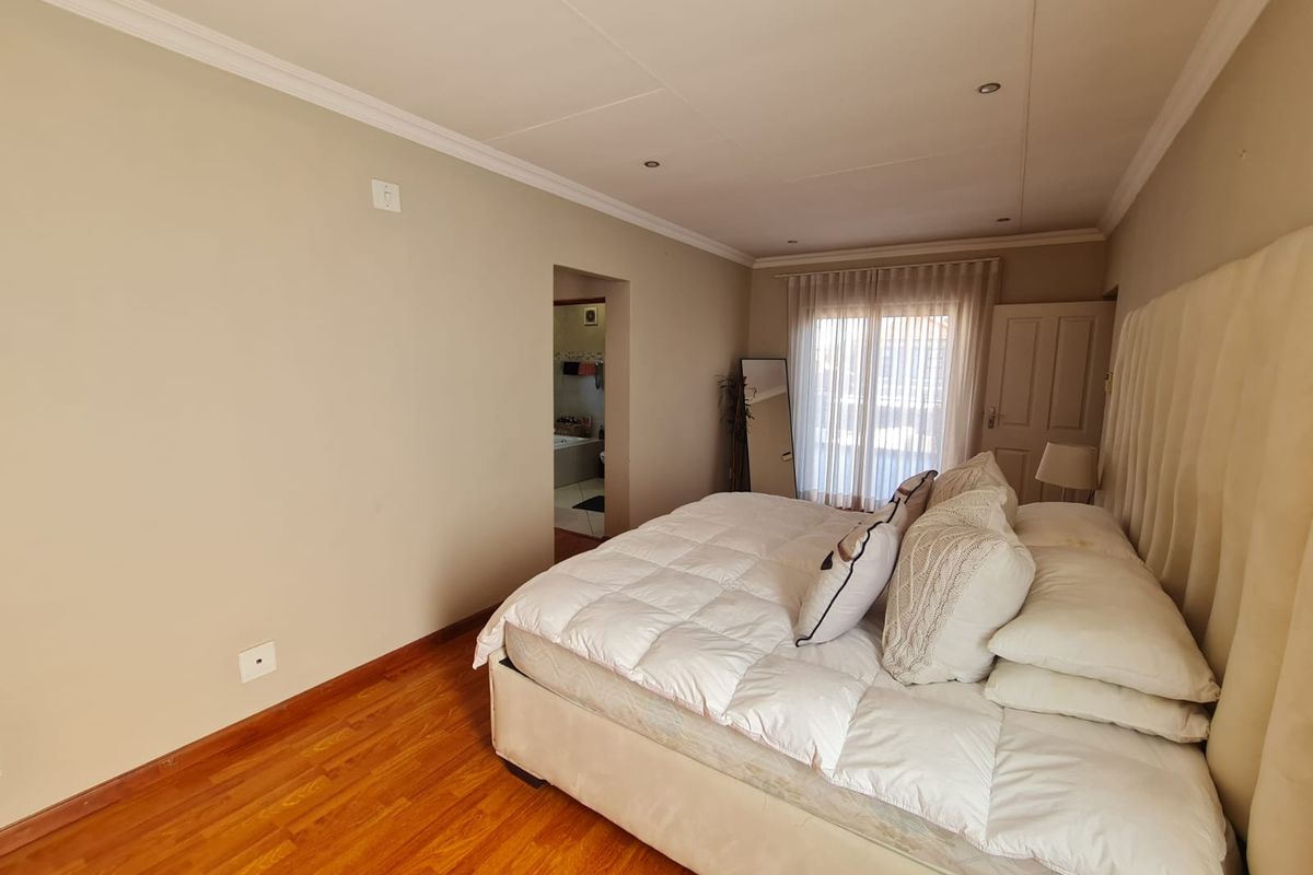 Spacious bedroom featuring warm laminate flooring, recessed lighting, and direct access to an en-suite bathroom through a connecting doorway.