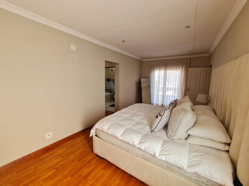 Spacious bedroom featuring warm laminate flooring, recessed lighting, and direct access to an en-suite bathroom through a connecting doorway.