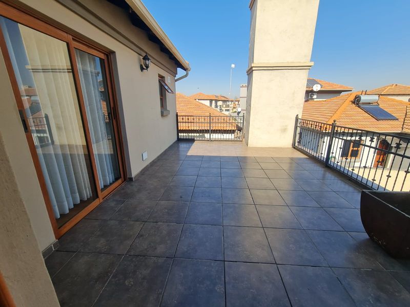 A spacious, tiled balcony featuring a wrought iron balustrade, sliding door access, and an integrated chimney stack, offering an open outdoor living area.