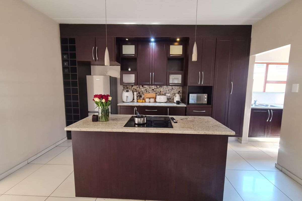 A modern kitchen featuring dark wood cabinetry, granite countertops, a central island with an integrated hob, and tiled flooring.