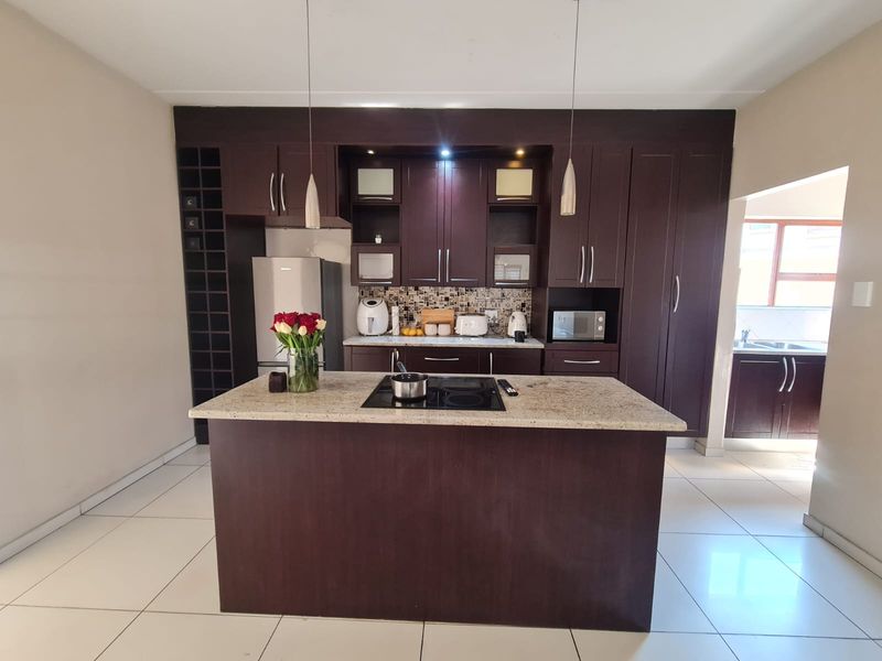 A modern kitchen featuring dark wood cabinetry, granite countertops, a central island with an integrated hob, and tiled flooring.