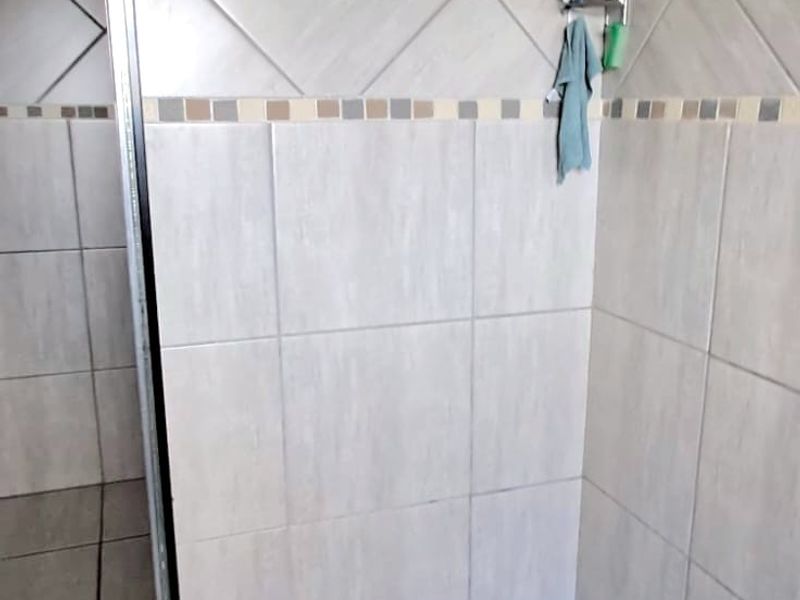 A walk-in shower featuring neutral wall tiles, a mosaic tiled floor, and a modern square shower head.