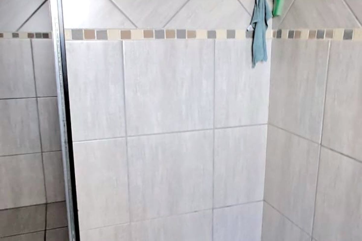 A walk-in shower featuring neutral wall tiles, a mosaic tiled floor, and a modern square shower head.