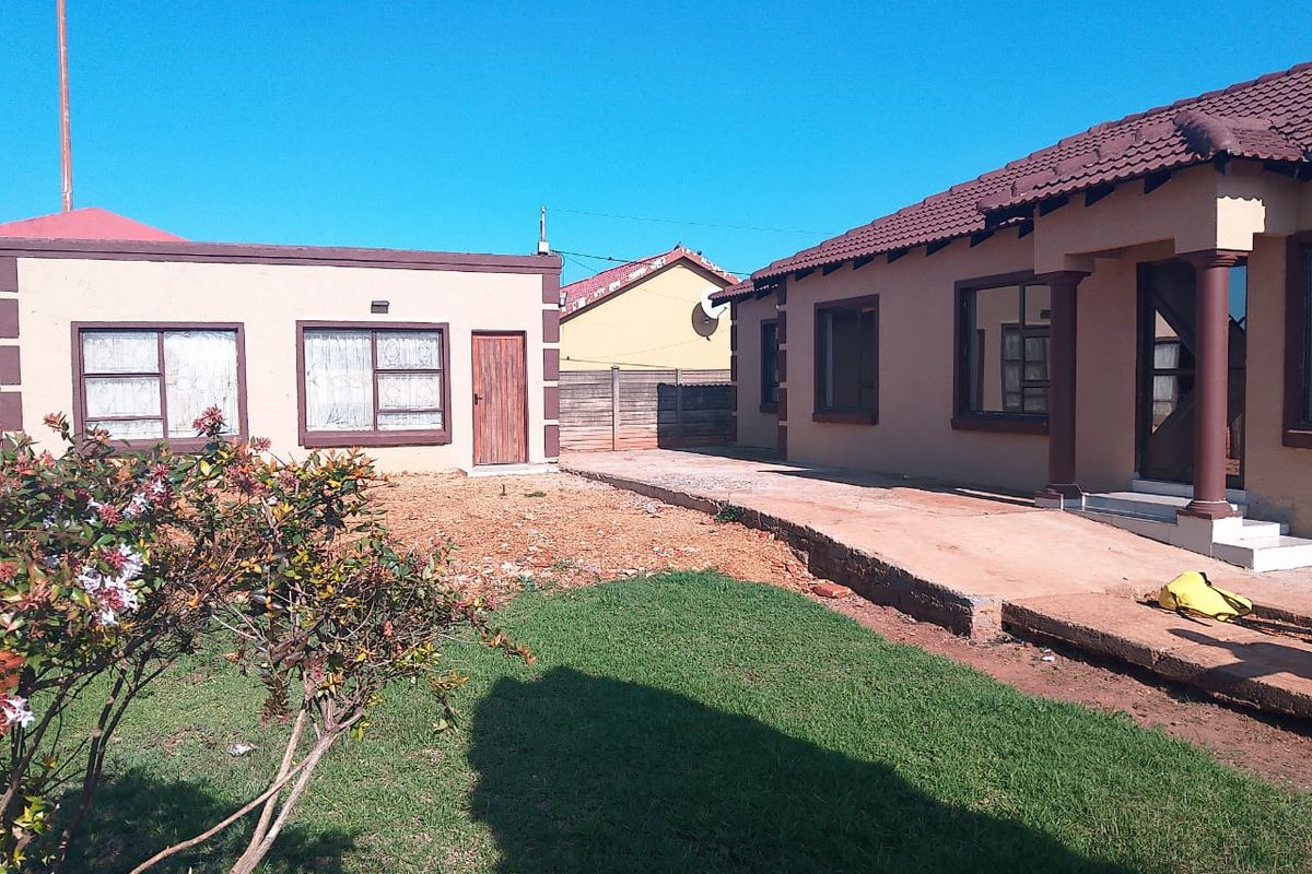 Rear view of the property featuring a tiled roof, concrete patio area, and a partially landscaped garden with boundary walling.