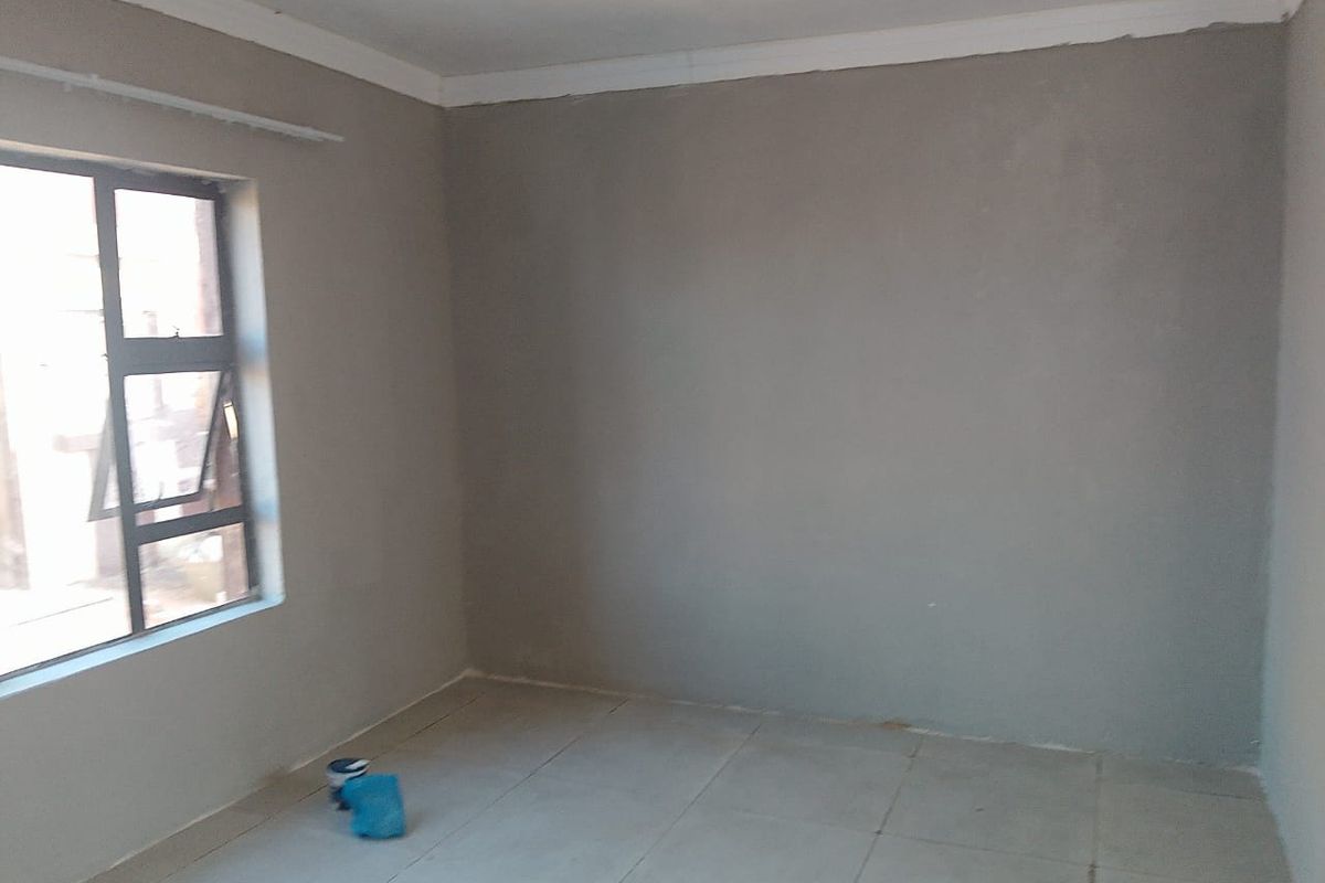 An empty bedroom featuring tiled flooring and an aluminium window frame, currently undergoing renovation with unfinished wall surfaces.