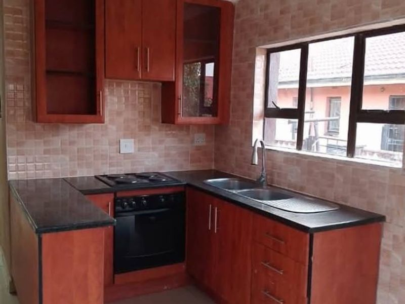 A functional kitchen featuring wooden cabinetry, granite countertops, a built-in oven and hob, and a tiled backsplash with a window view.