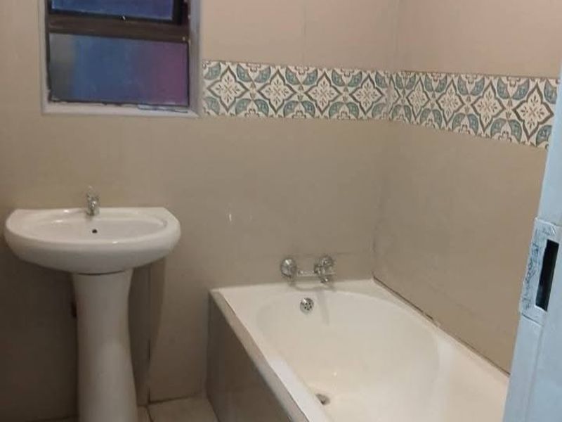 A clean, functional bathroom featuring a pedestal basin, a built-in bathtub, and decorative tiled wall accents.
