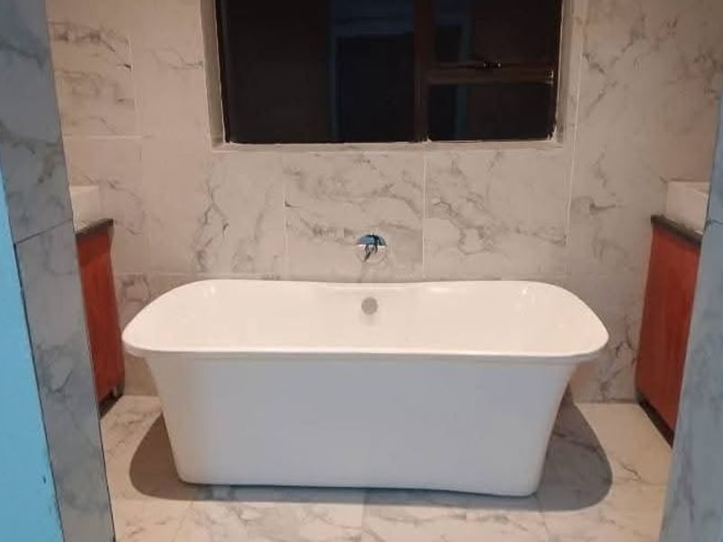 A modern bathroom featuring a freestanding bathtub, marble-look wall and floor tiling, and dual vanity cabinets.