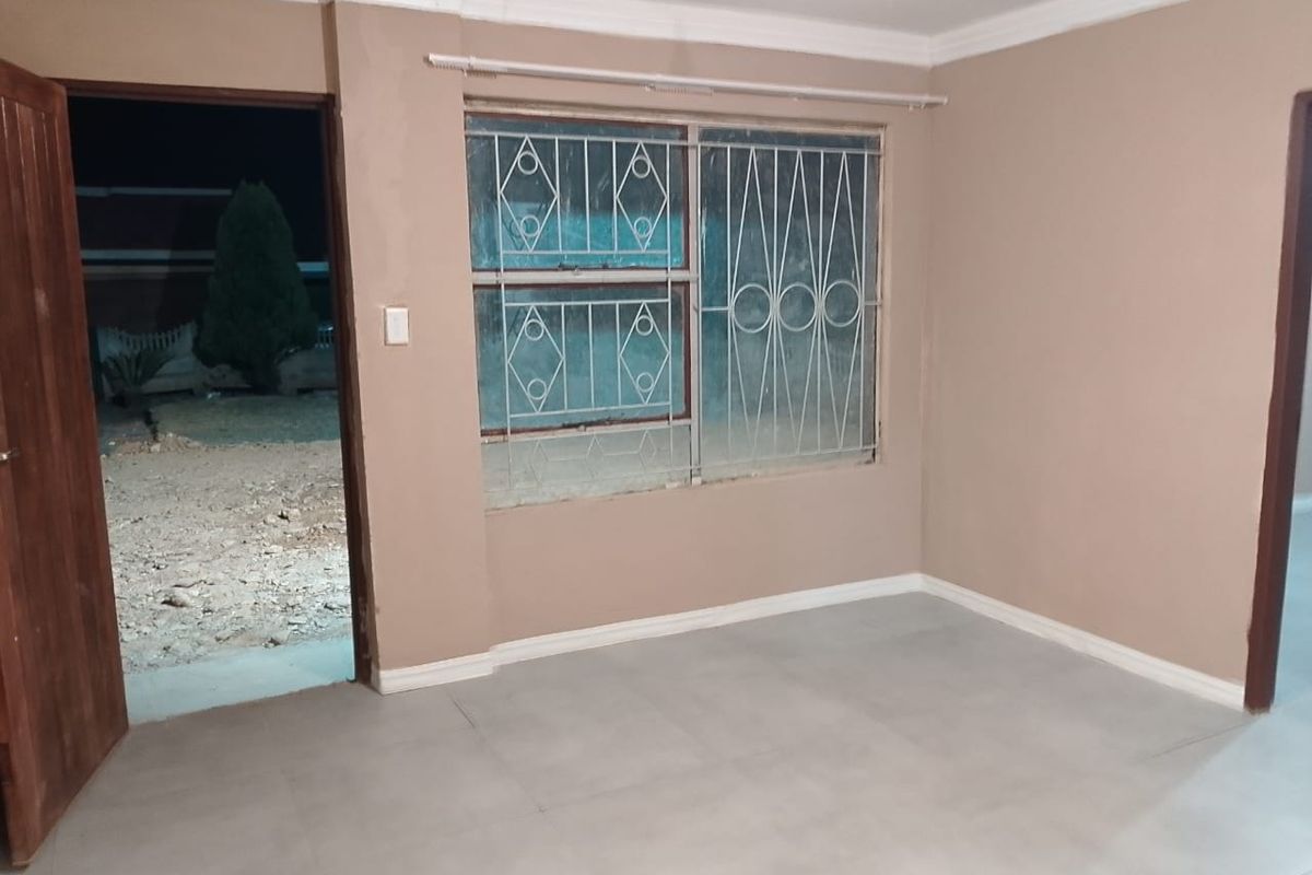 An empty living room featuring tiled flooring, coving, and security bars on the window, with direct access to the exterior.