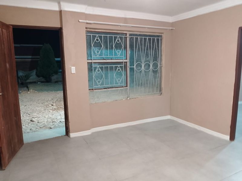 An empty living room featuring tiled flooring, coving, and security bars on the window, with direct access to the exterior.