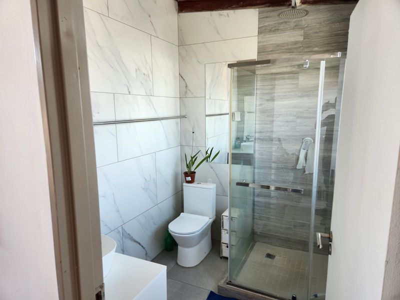 Modern bathroom featuring a walk-in shower with a rain shower head, glass enclosure, and contemporary marble-look wall tiling.
