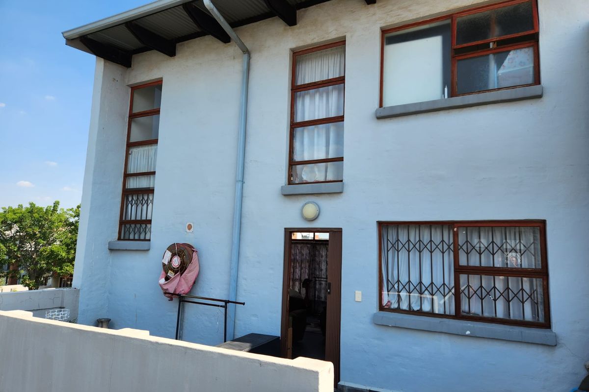 Rear elevation of a two-story flat featuring timber-framed windows with security gates, exposed roof rafters, and a paved outdoor area.