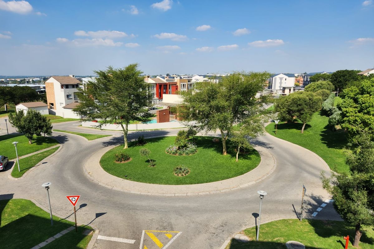 An elevated aerial view of a residential estate roundabout featuring landscaped green spaces, paved roads, and surrounding residential buildings.