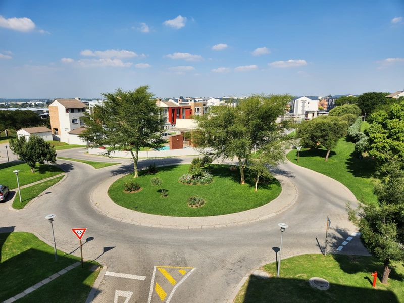 An elevated aerial view of a residential estate roundabout featuring landscaped green spaces, paved roads, and surrounding residential buildings.