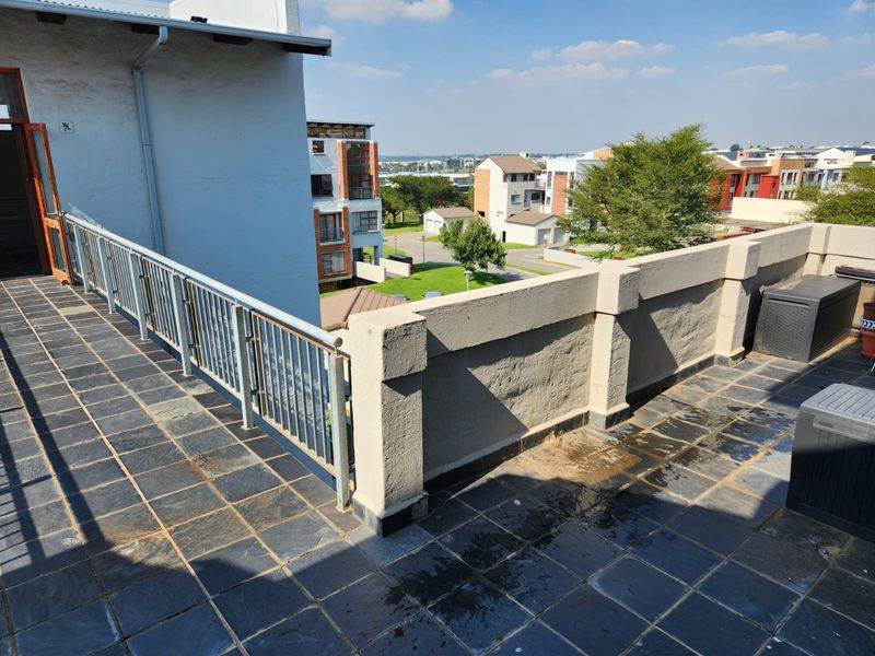 Spacious open-air balcony featuring slate tile flooring, a metal safety balustrade, and a masonry parapet wall with views of the surrounding residential complex.