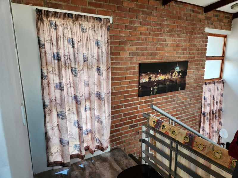 A hallway area featuring an exposed brick wall, metal staircase railing, and timber-framed windows, providing a rustic industrial aesthetic.