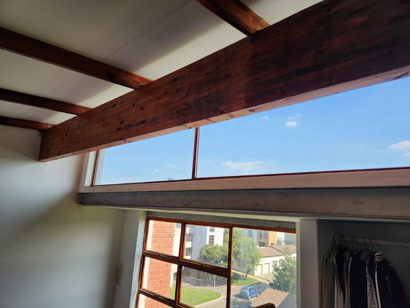 Bedroom featuring exposed timber ceiling beams, clerestory windows for natural light, and a built-in wardrobe with views of the surrounding area.