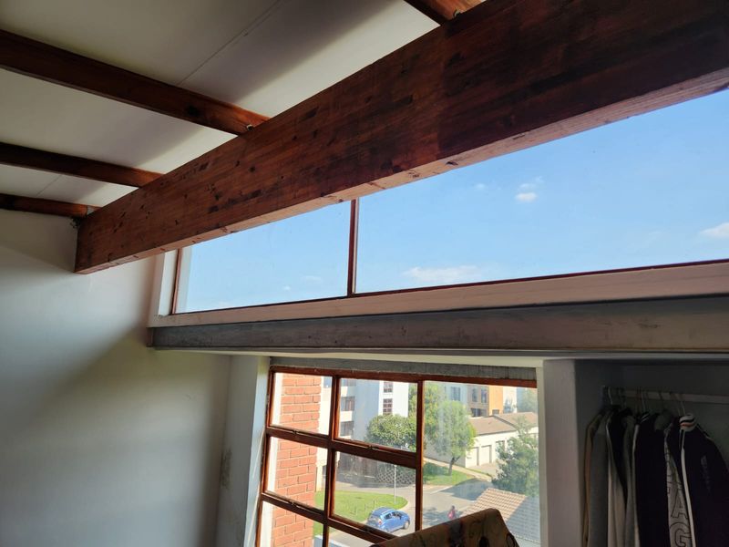 Bedroom featuring exposed timber ceiling beams, clerestory windows for natural light, and a large multi-pane window overlooking the street.