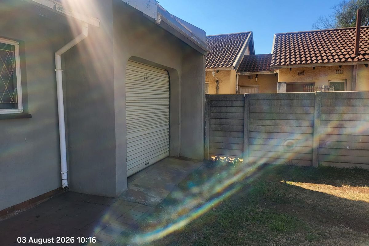 Rear exterior view showing a single garage with a roller door, adjacent precast concrete boundary wall, and paved access area.