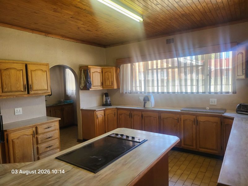 A dated kitchen featuring timber cabinetry, a central island with a built-in hob, timber ceiling, and tiled flooring, offering potential for modernization.