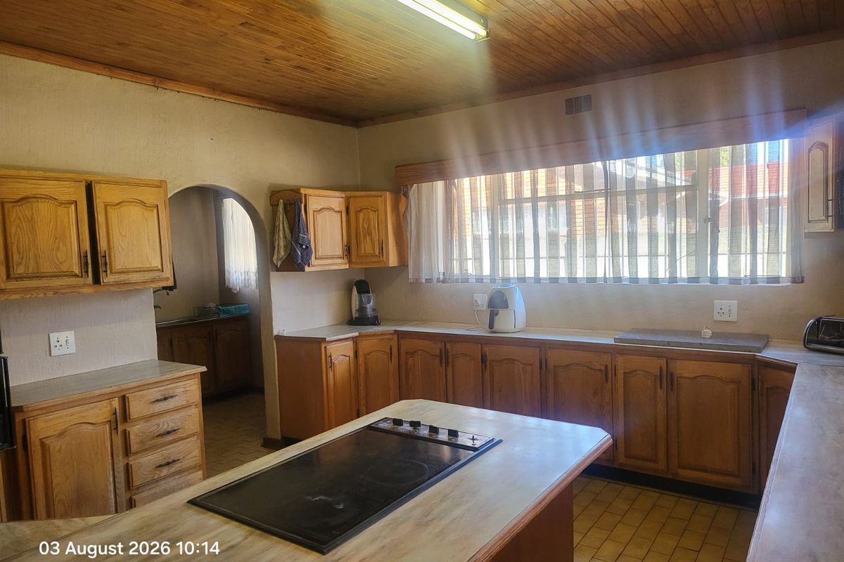 A dated kitchen featuring timber cabinetry, a central island with a built-in hob, timber ceiling, and tiled flooring, offering potential for modernization.