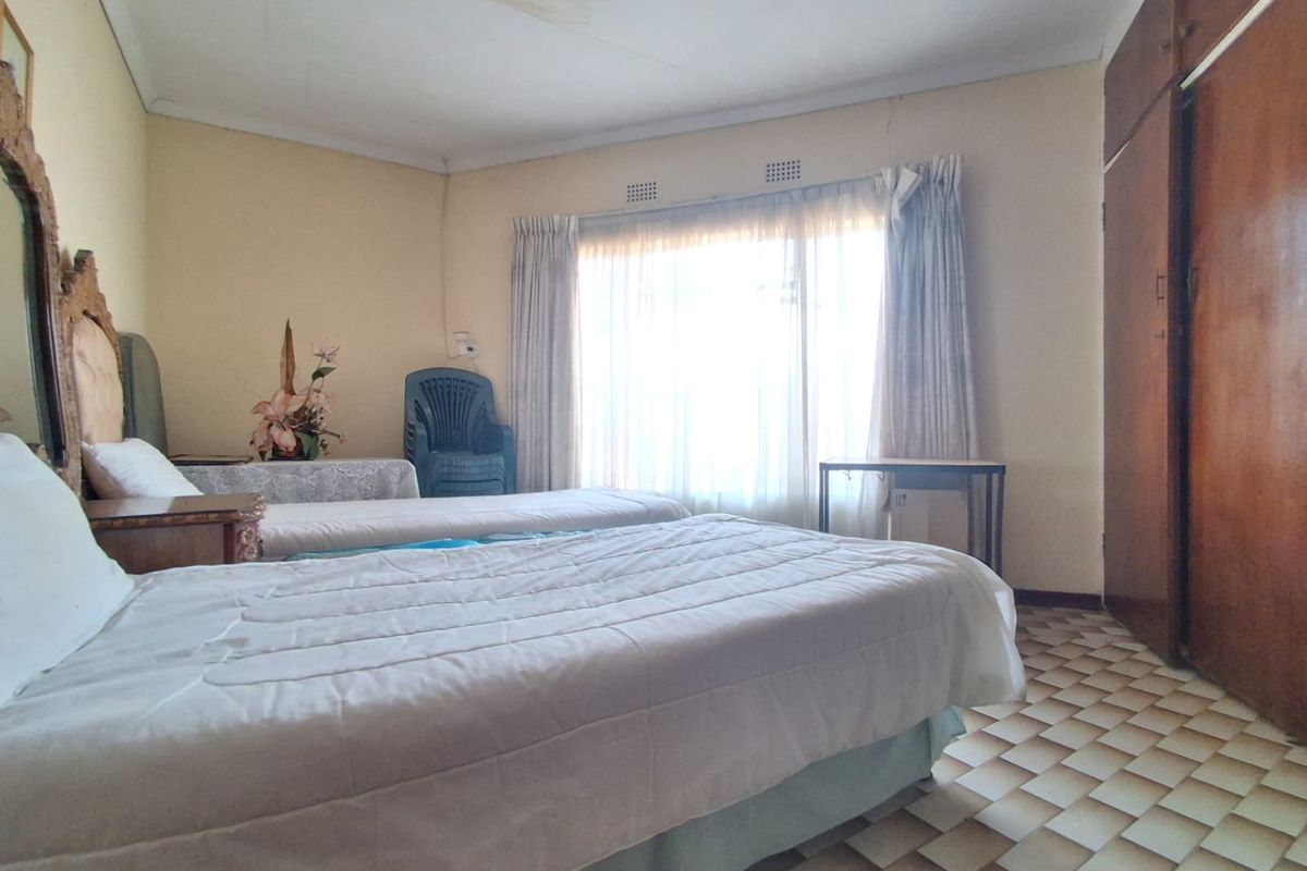 A bedroom featuring built-in cupboards, tiled flooring, and large windows with curtain rails. The room shows signs of ceiling water damage and dated finishes.