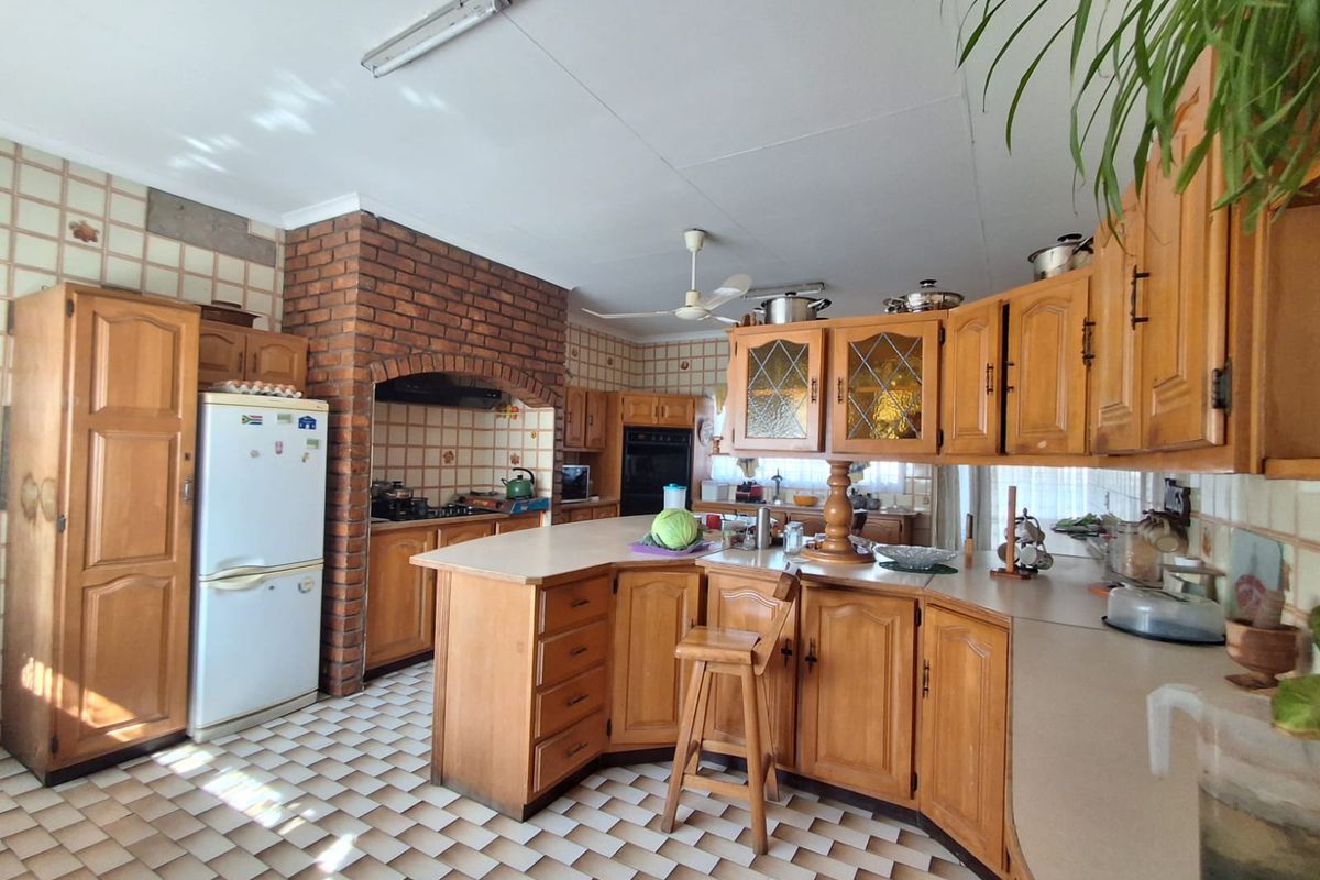 Spacious kitchen featuring wooden cabinetry, a brick feature wall, built-in oven, and hob, offering a traditional layout with ample storage and counter space.