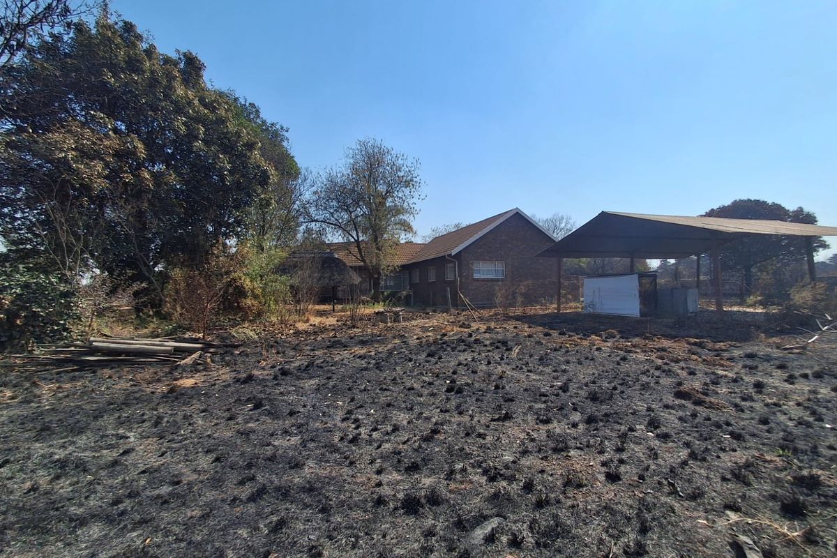 Rear view of a brick house featuring a carport and extensive grounds showing signs of recent fire damage to the vegetation.