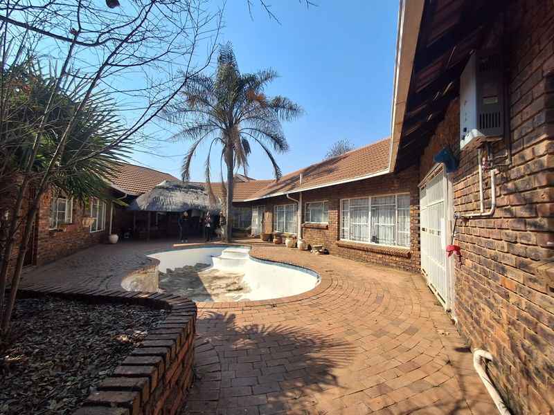 Outdoor pool area featuring brick paving, a thatch lapa, and an empty swimming pool requiring maintenance.