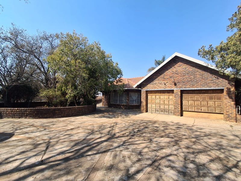 Front exterior view of a face brick house featuring a double garage and a large concrete driveway surrounded by mature trees.