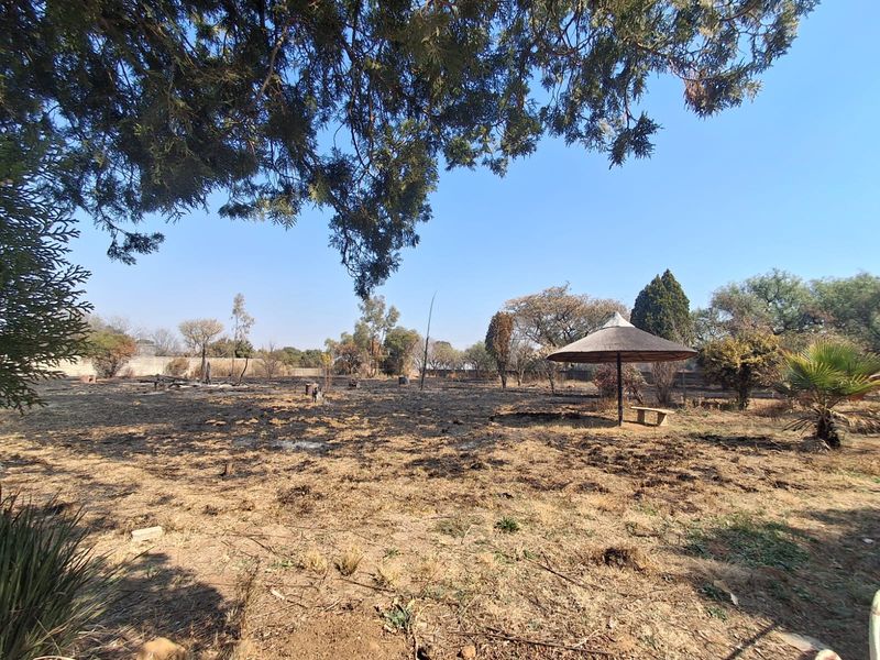 Large outdoor garden area featuring a thatched lapa structure, currently showing significant signs of fire damage to the surrounding landscape.
