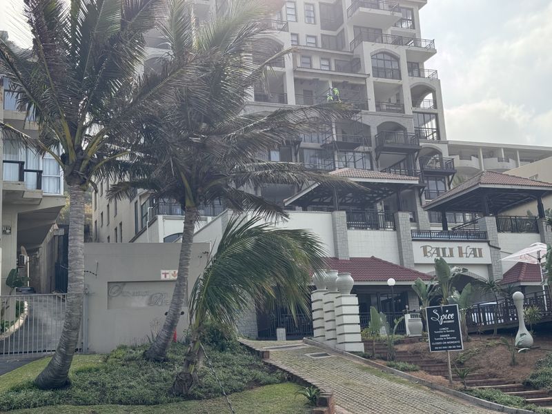 Exterior view of a multi-story apartment complex featuring balconies, landscaped grounds, and a paved entrance driveway.