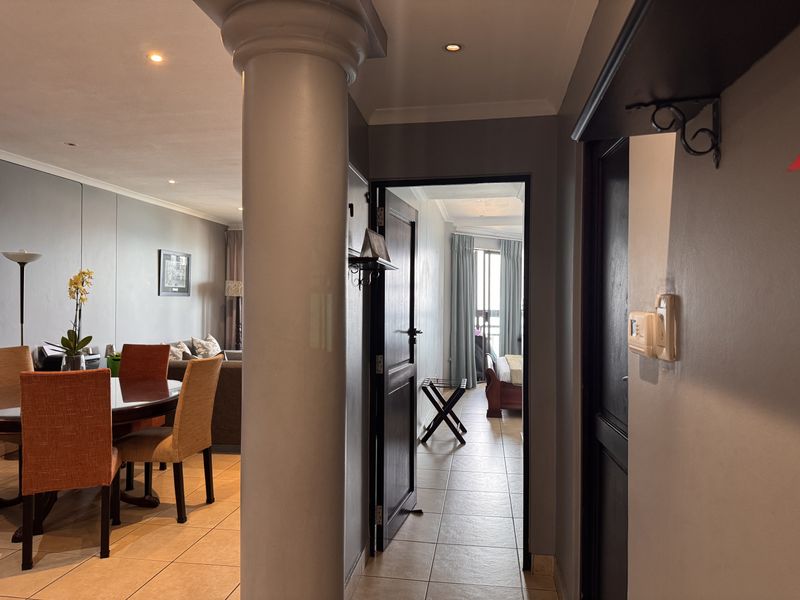 A view from the hallway looking into the dining area and a bedroom, featuring tiled flooring and a prominent structural column.