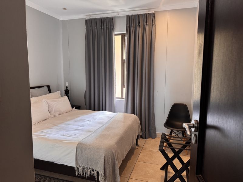 A well-maintained bedroom featuring neutral wall tones, tiled flooring, and natural light through a window with floor-to-ceiling curtains.