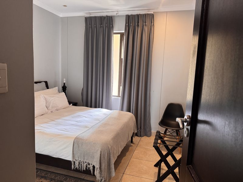 A well-maintained bedroom featuring neutral wall tones, tiled flooring, and floor-to-ceiling curtains providing natural light control.