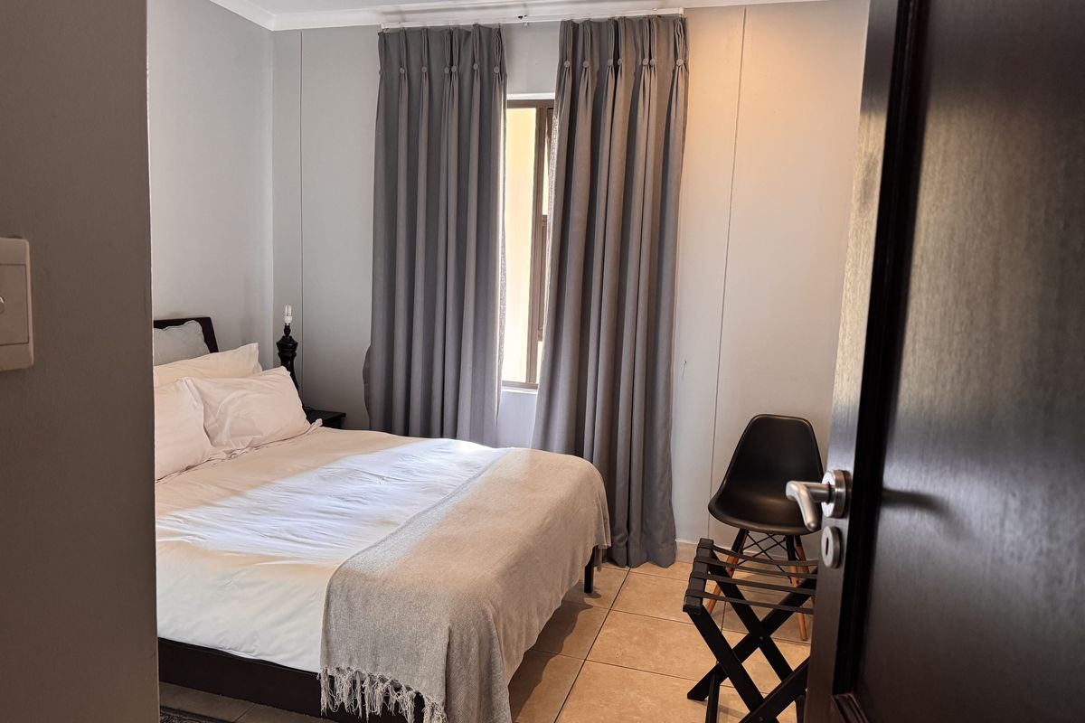 A well-maintained bedroom featuring neutral wall tones, tiled flooring, and floor-to-ceiling curtains providing natural light control.